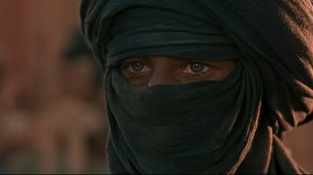 Movie still from “The Sheltering Sky” (1990), directed by Bernardo Bertolucci – A man with a black head covering and green eyes; Close Up shot, Over the shoulder angle
