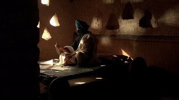 Movie still from “The Sheltering Sky” (1990), directed by Bernardo Bertolucci – A man sitting on a bed reading a book; Wide shot, Low angle