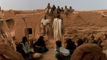 Movie still from “The Sheltering Sky” (1990), directed by Bernardo Bertolucci – A group of people sitting and standing on a dirt hill; Wide shot, Low angle