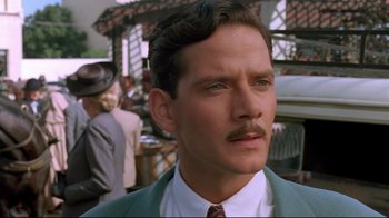 Movie still from “The Sheltering Sky” (1990), directed by Bernardo Bertolucci – A man with a mustache in a green suit; Close Up shot, Low angle