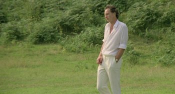 Movie still from “The Shout” (1978), directed by Jerzy Skolimowski – A man in a white shirt is standing in the grass; Medium shot, Low angle