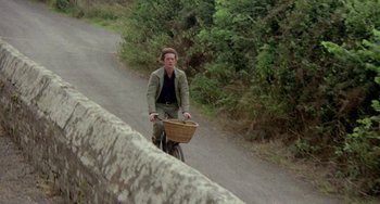 Movie still from “The Shout” (1978), directed by Jerzy Skolimowski – A man riding a bike down a road with trees in the background; Wide shot, High angle