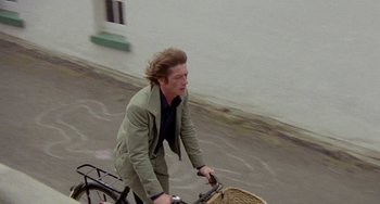 Movie still from “The Shout” (1978), directed by Jerzy Skolimowski – A man riding a bike down a street; Medium shot, High angle