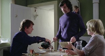 Movie still from “The Shout” (1978), directed by Jerzy Skolimowski – A group of people sitting at a table with plates of food; Medium shot, Over the shoulder angle
