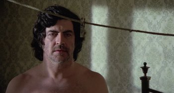 Movie still from “The Shout” (1978), directed by Jerzy Skolimowski – A man with a beard and mustache is standing in front of a curtain; Close Up shot, Low angle