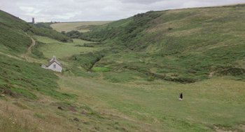 Movie still from “The Shout” (1978), directed by Jerzy Skolimowski – A person standing in a field near a body of water; Extreme Wide shot, High angle