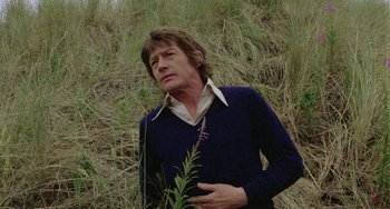 Movie still from “The Shout” (1978), directed by Jerzy Skolimowski – A man standing in the grass holding a plant; Medium shot, Low angle