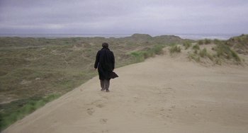 Movie still from “The Shout” (1978), directed by Jerzy Skolimowski – A man walking down a dirt path on a beach; Extreme Wide shot, High angle