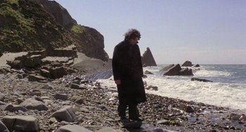 Movie still from “The Shout” (1978), directed by Jerzy Skolimowski – A man standing on a rocky beach near the ocean; Wide shot, Low angle