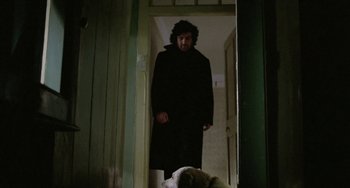 Movie still from “The Shout” (1978), directed by Jerzy Skolimowski – A man in a black coat walking down a hall way; Medium shot, Low angle