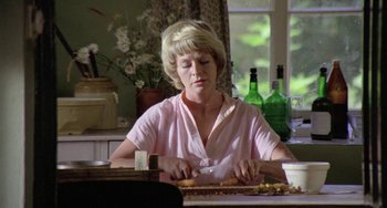 Movie still from “The Shout” (1978), directed by Jerzy Skolimowski – A woman sitting at a table cutting a piece of cake; Medium shot, Low angle