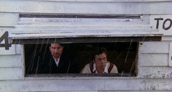 Movie still from “The Shout” (1978), directed by Jerzy Skolimowski – Two men looking out of a window on a rainy day; Medium shot, High angle