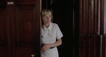 Movie still from “The Shout” (1978), directed by Jerzy Skolimowski – A woman standing in front of a door holding a cell phone; Medium shot, Low angle