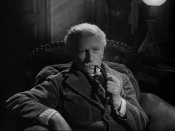 Movie still from “The Silence of the Sea” (1949), directed by Jean-Pierre Melville – An older man sitting in a chair with a pipe in his mouth; Medium shot, High angle