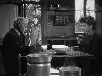 Movie still from “The Silence of the Sea” (1949), directed by Jean-Pierre Melville – Two people sitting at a table with a person standing next to them; Medium shot, Over the shoulder angle