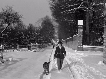 Movie still from “The Silence of the Sea” (1949), directed by Jean-Pierre Melville – A woman walking a dog down a snow covered street; Wide shot, High angle
