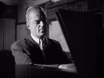 Movie still from “The Silence of the Sea” (1949), directed by Jean-Pierre Melville – A man in a suit and tie sitting at a piano; Close Up shot, Low angle