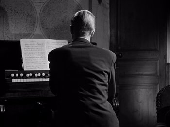 Movie still from “The Silence of the Sea” (1949), directed by Jean-Pierre Melville – A man in a suit sitting in front of an organ keyboard; Medium shot, Over the shoulder angle
