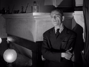 Movie still from “The Silence of the Sea” (1949), directed by Jean-Pierre Melville – A man in a suit and tie standing in front of a fireplace; Medium shot, Low angle