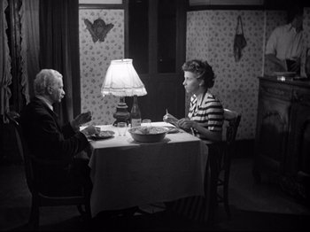Movie still from “The Silence of the Sea” (1949), directed by Jean-Pierre Melville – Two people sitting at a table in front of a lamp; Medium shot, High angle