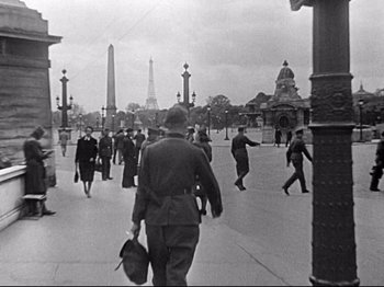 Movie still from “The Silence of the Sea” (1949), directed by Jean-Pierre Melville – A black and white photo of people walking down a street; Extreme Wide shot, High angle