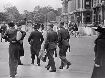 Movie still from “The Silence of the Sea” (1949), directed by Jean-Pierre Melville – A black and white photo of men walking down a street; Wide shot, Over the shoulder angle