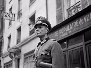 Movie still from “The Silence of the Sea” (1949), directed by Jean-Pierre Melville – A man in a military uniform standing in front of a building; Medium shot, Low angle