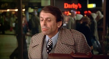 Movie still from “The Silent Partner” (1978), directed by Daryl Duke – A man wearing a suit and tie sitting down; Close Up shot, Over the shoulder angle