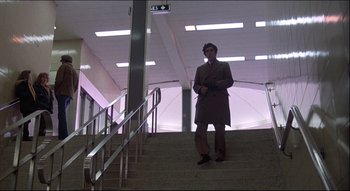 Movie still from “The Silent Partner” (1978), directed by Daryl Duke – A man in a long coat standing on a set of stairs; Wide shot, Low angle
