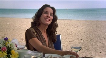 Movie still from “The Silent Partner” (1978), directed by Daryl Duke – A woman sitting at a table on the beach; Close Up shot, Low angle
