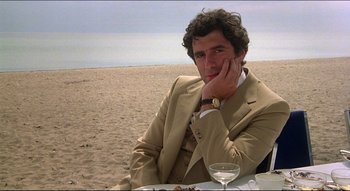 Movie still from “The Silent Partner” (1978), directed by Daryl Duke – A man sitting at a table on the beach; Medium shot, Over the shoulder angle