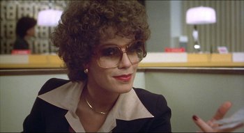 Movie still from “The Silent Partner” (1978), directed by Daryl Duke – A person wearing glasses and a suit; Close Up shot, Over the shoulder angle