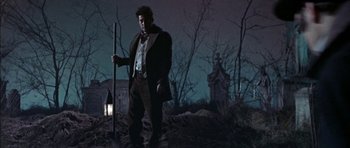 Movie still from “The Skull” (1965), directed by Freddie Francis – A man holding a stick standing in the dark; Wide shot, Low angle
