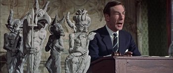 Movie still from “The Skull” (1965), directed by Freddie Francis – A man in a suit and tie standing at a podium; Close Up shot, Low angle