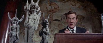 Movie still from “The Skull” (1965), directed by Freddie Francis – A man is giving a lecture in front of statues; Medium shot, Low angle