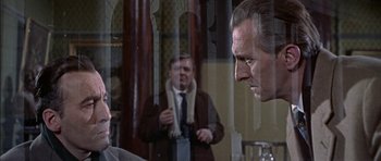 Movie still from “The Skull” (1965), directed by Freddie Francis – A man in a suit and tie looking at another man in a suit and tie in front of a mirror; Medium shot, Over the shoulder angle