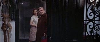 Movie still from “The Skull” (1965), directed by Freddie Francis – A man and a woman standing next to each other in front of a curtain; Medium shot, Low angle