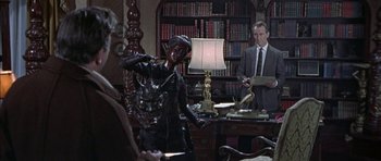 Movie still from “The Skull” (1965), directed by Freddie Francis – A man in a suit and tie standing in front of a woman; Medium shot, Over the shoulder angle