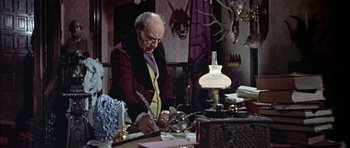 Movie still from “The Skull” (1965), directed by Freddie Francis – An old man writing on a piece of paper in front of a lamp; Medium shot, High angle