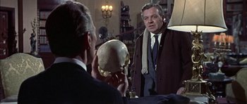 Movie still from “The Skull” (1965), directed by Freddie Francis – A man holding a skull in front of another man; Close Up shot, Over the shoulder angle