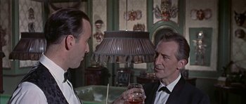 Movie still from “The Skull” (1965), directed by Freddie Francis – Two men in suits are holding wine glasses in a room; Close Up shot, Over the shoulder angle