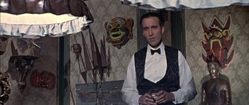 Movie still from “The Skull” (1965), directed by Freddie Francis – A man wearing a vest and bow tie holding a drink; Medium shot, Over the shoulder angle
