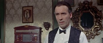 Movie still from “The Skull” (1965), directed by Freddie Francis – A person wearing a suit and bow tie; Close Up shot, Over the shoulder angle