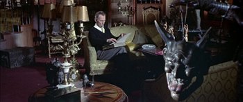 Movie still from “The Skull” (1965), directed by Freddie Francis – A man sitting on top of a couch in a living room; Medium shot, High angle