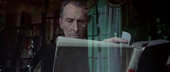 Movie still from “The Skull” (1965), directed by Freddie Francis – A man reading a newspaper through a glass window; Close Up shot, Over the shoulder angle
