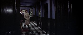 Movie still from “The Skull” (1965), directed by Freddie Francis – A man wearing a trench coat and hat in a hallway; Wide shot, High angle