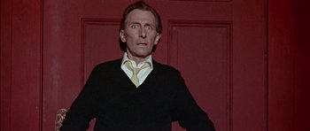 Movie still from “The Skull” (1965), directed by Freddie Francis – A man standing in front of a red wall wearing a tie; Medium shot, Low angle