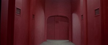 Movie still from “The Skull” (1965), directed by Freddie Francis – An empty room with a red wall and an arched doorway; Extreme Wide shot, High angle