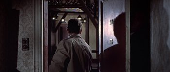 Movie still from “The Skull” (1965), directed by Freddie Francis – A man standing next to a door in a room; Medium shot, Over the shoulder angle