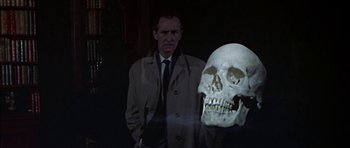 Movie still from “The Skull” (1965), directed by Freddie Francis – A man standing next to a skull in a dark room; Close Up shot, Over the shoulder angle